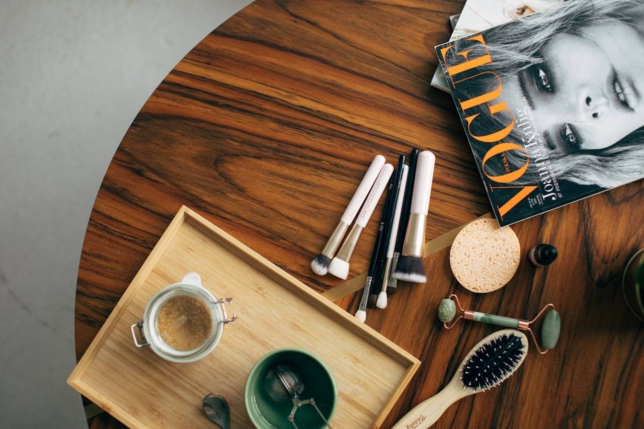 Stylish flatlay featuring makeup brushes, a Vogue magazine, and a coffee cup on a wooden table.